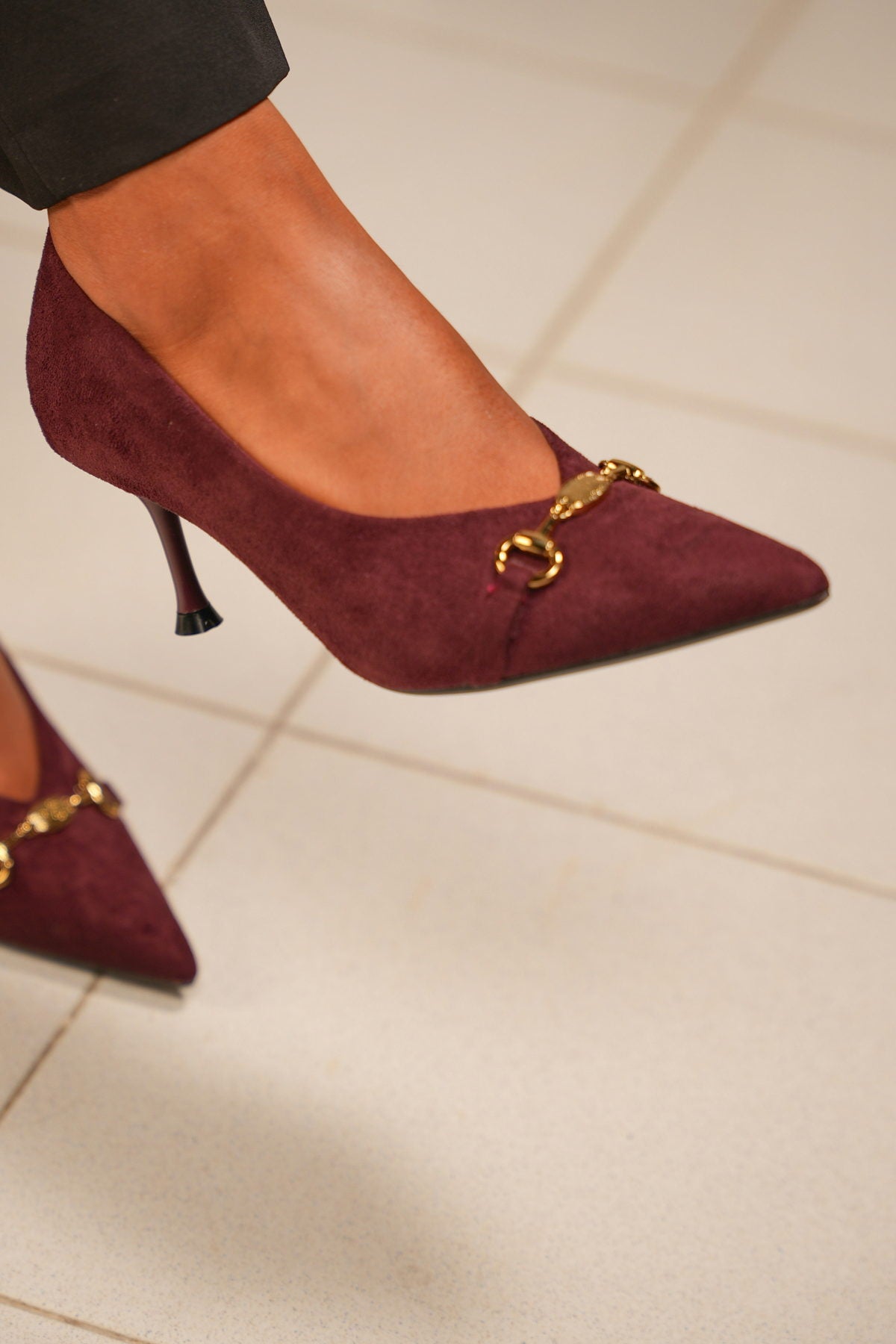 Burgundy suede court shoes with a gold bit, worn with dark trousers